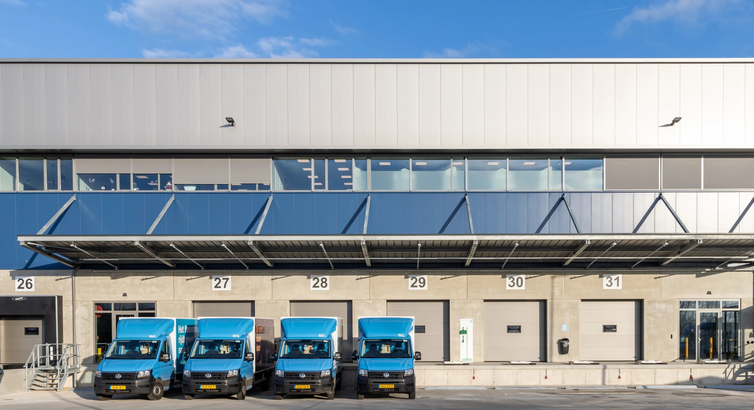 A row of blue delivery vans parked in front of a warehouse loading dock.