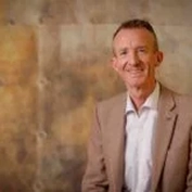 A man in a brown suit with a neutral background.