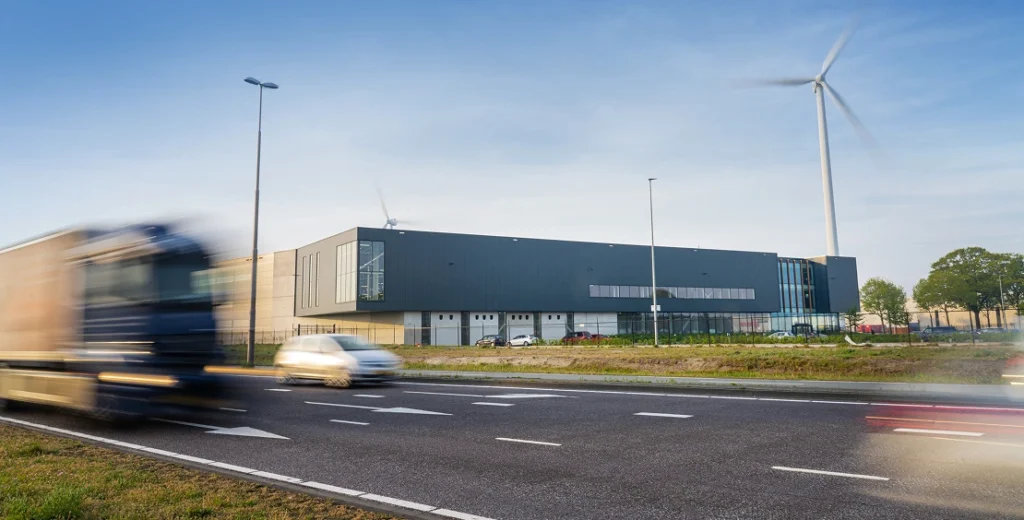 A modern industrial building with a wind turbine and vehicles speeding past.