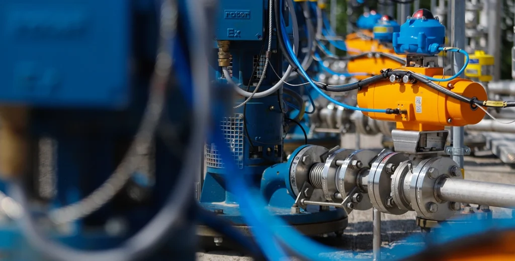 Rows of industrial pumps and pipes with coloured cabling.