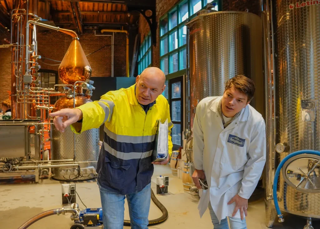 A Vicoma employee discusses operations with a customer in a facility with large metal tanks and equipment.