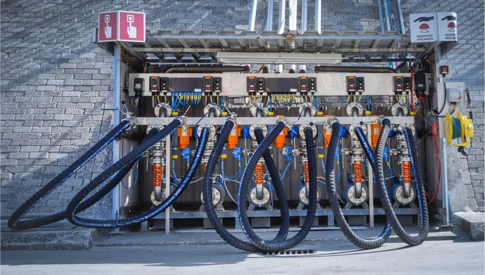 A row of industrial chemical connections and pipes mounted on a brick wall.