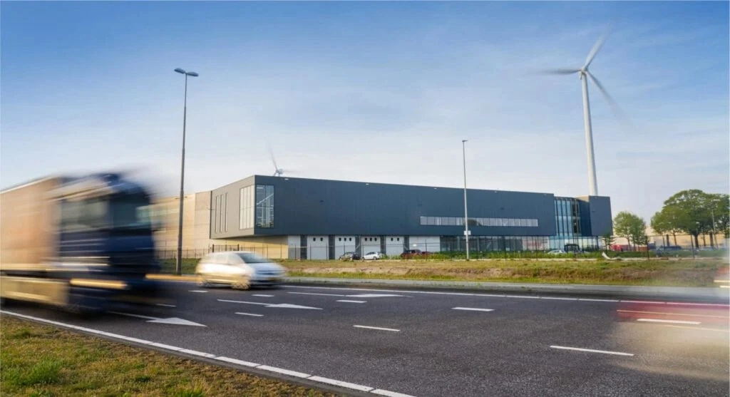A modern building with a wind turbine in the background and blurred vehicles passing on the road in the foreground.