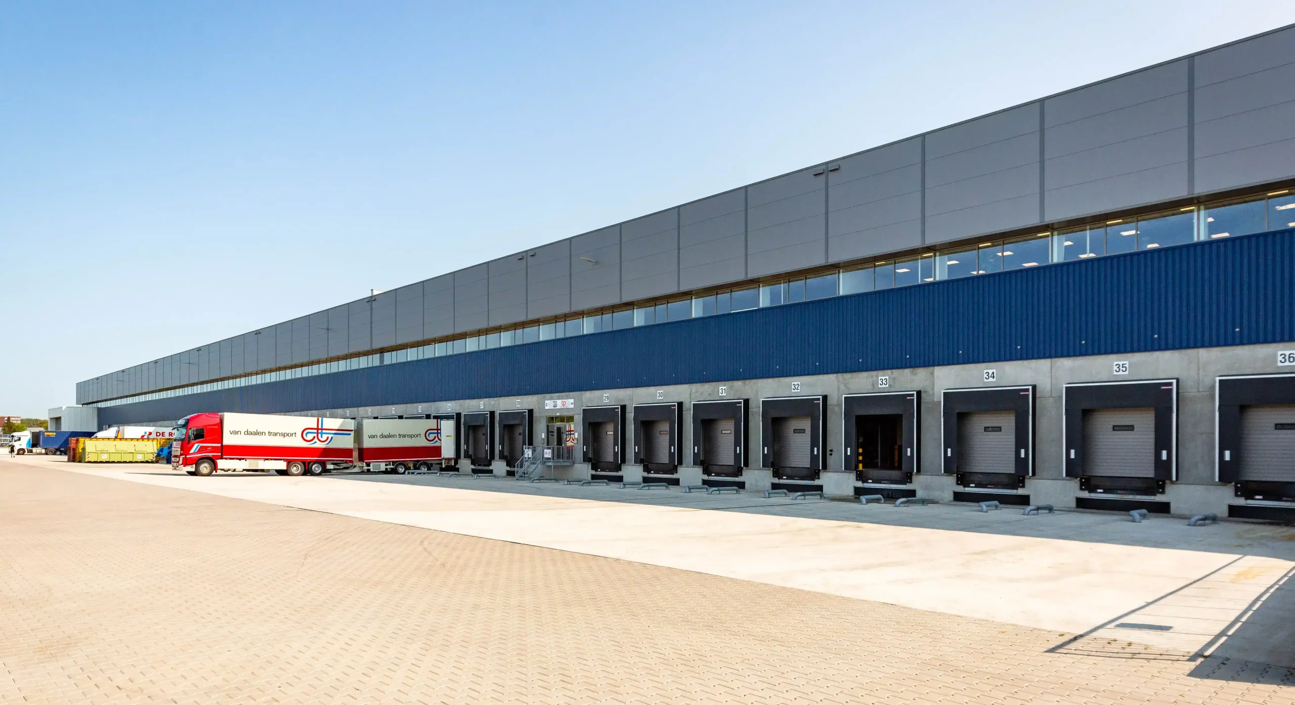 A warehouse loading dock with several cargo bays and a van Daalen transport truck parked.
