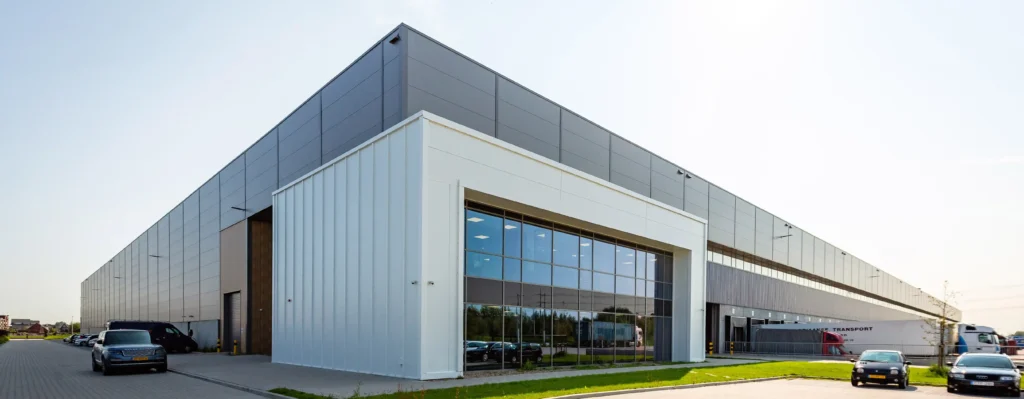 A large modern warehouse building with multiple parked vehicles in front.