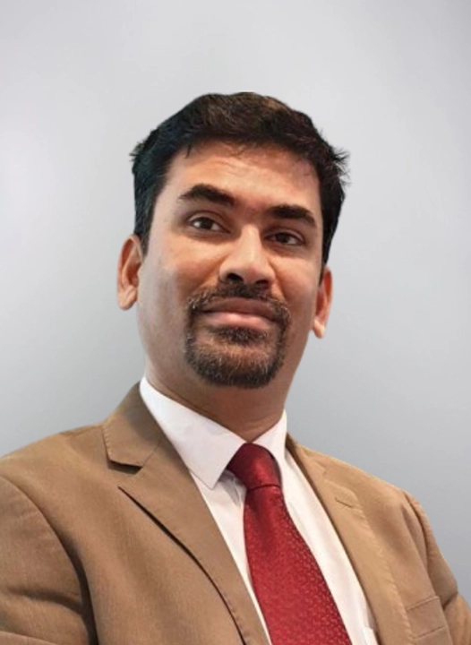 A man in a suit and tie looks slightly to the side against a neutral background.