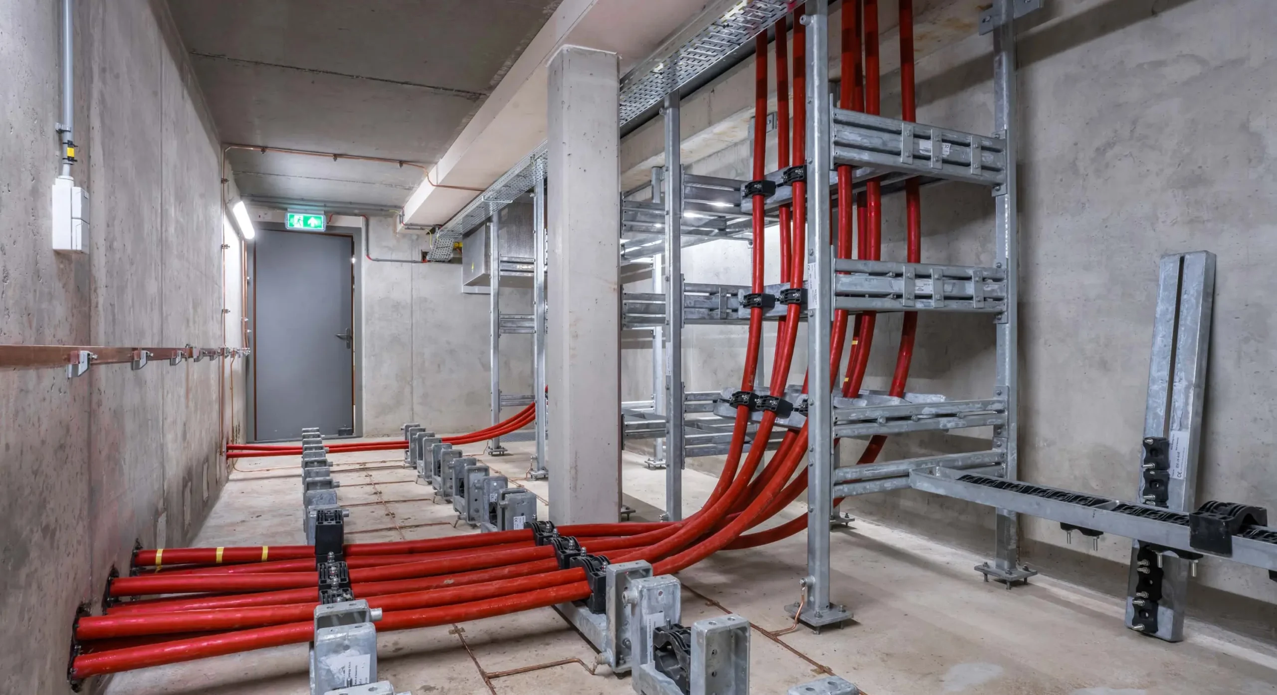 Utility room with red power cables and metal cable trays along the concrete walls and floor.