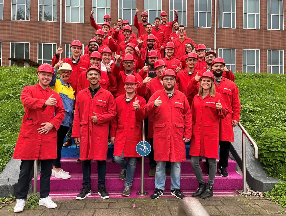 A group of people wearing red suits and helmets posing on colorful stairs with a building in the background.