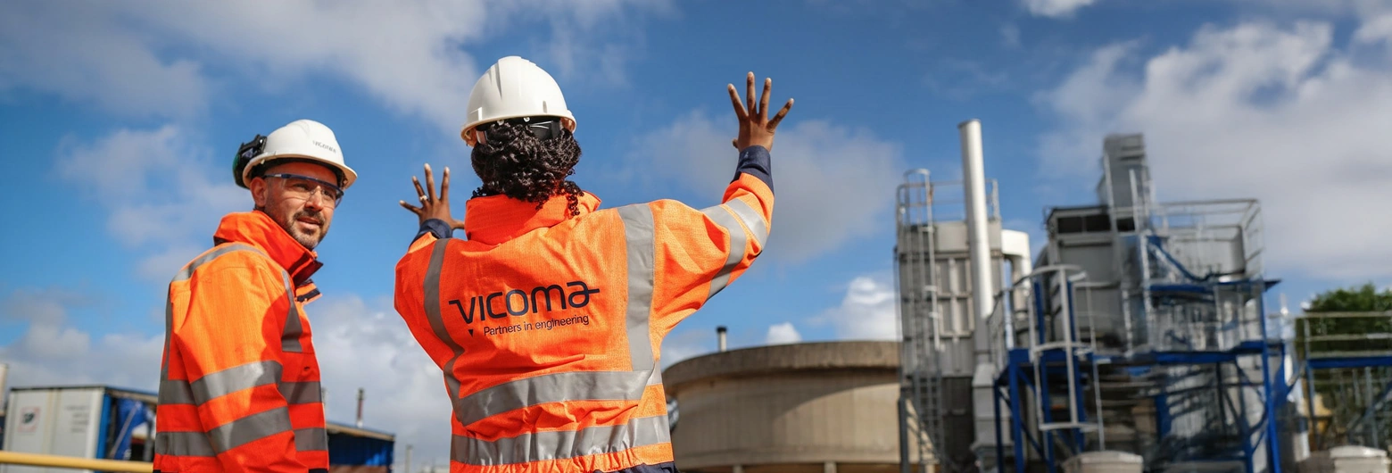 Two people wearing Vicoma-branded safety gear and helmets at an industrial site.