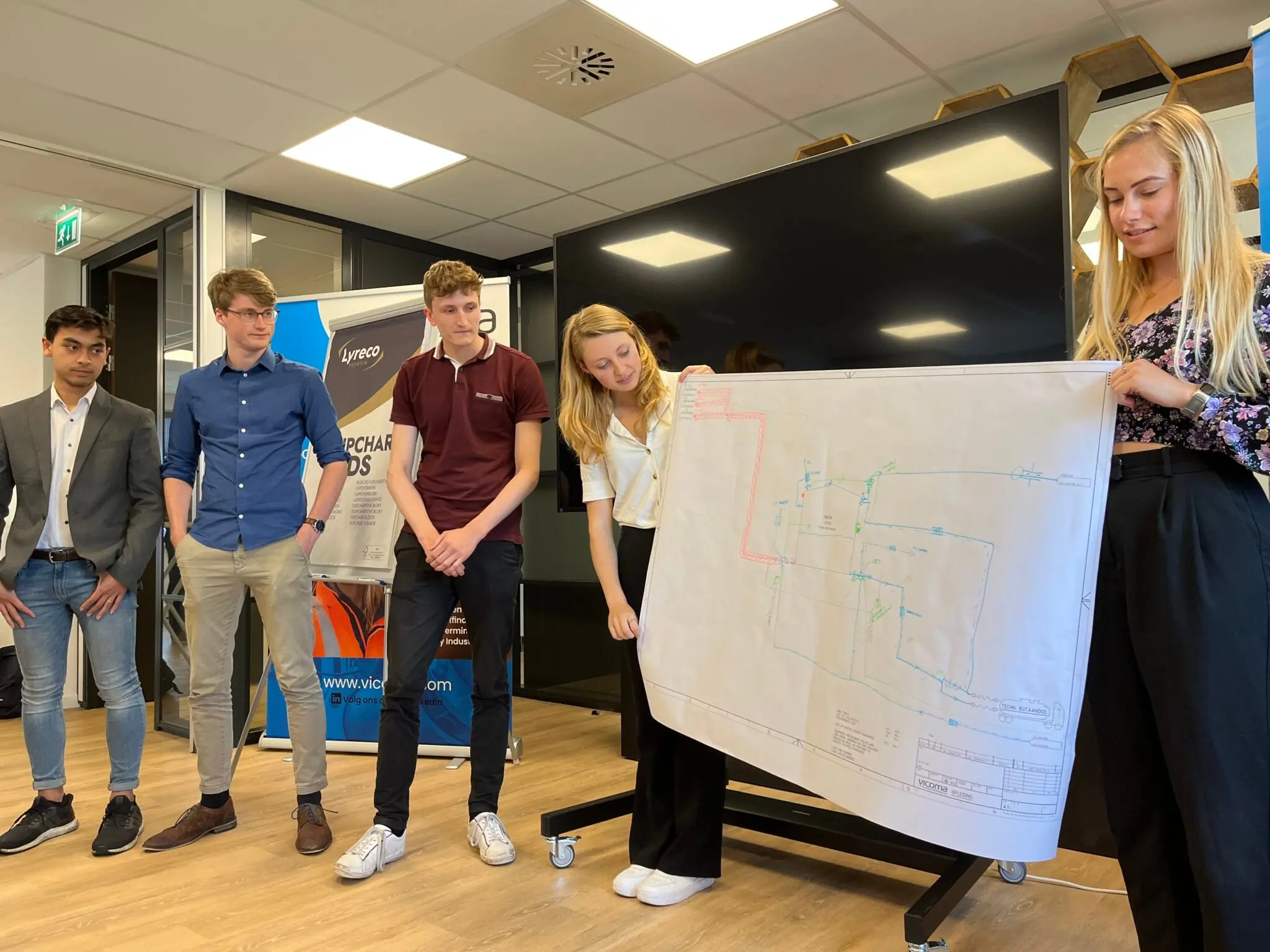 A group of students from the Vicoma study association are presenting a large technical diagram.